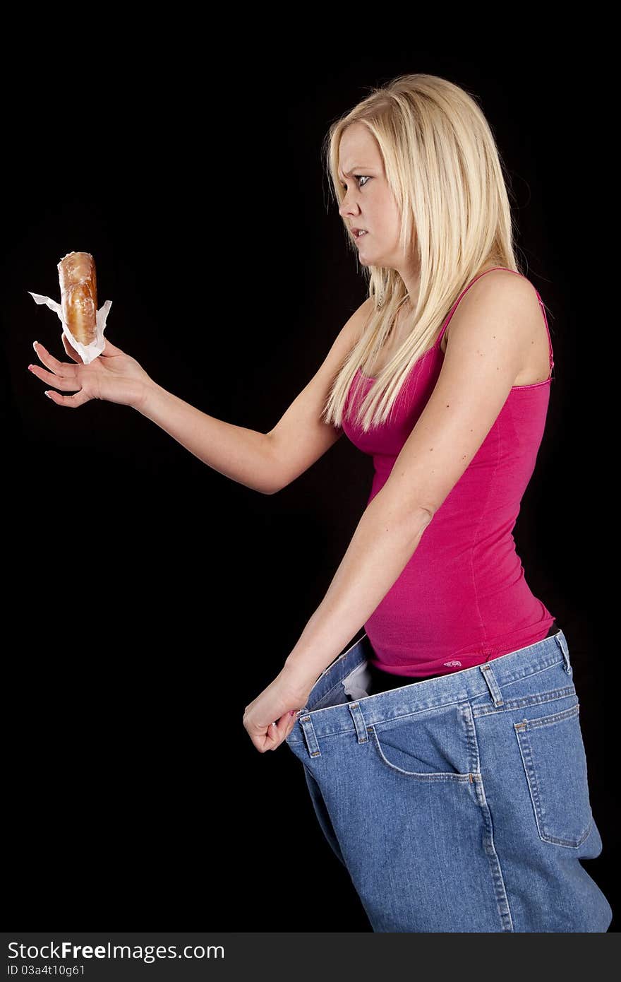 A woman with big pants is looking mad at a donut. A woman with big pants is looking mad at a donut