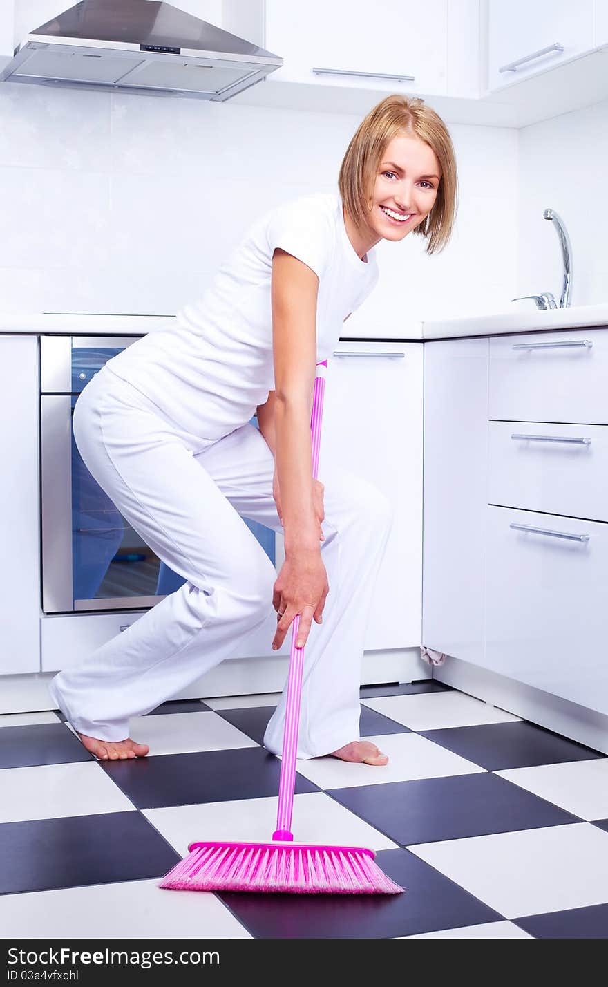 Beautiful young housewife with a broom in the kitchen