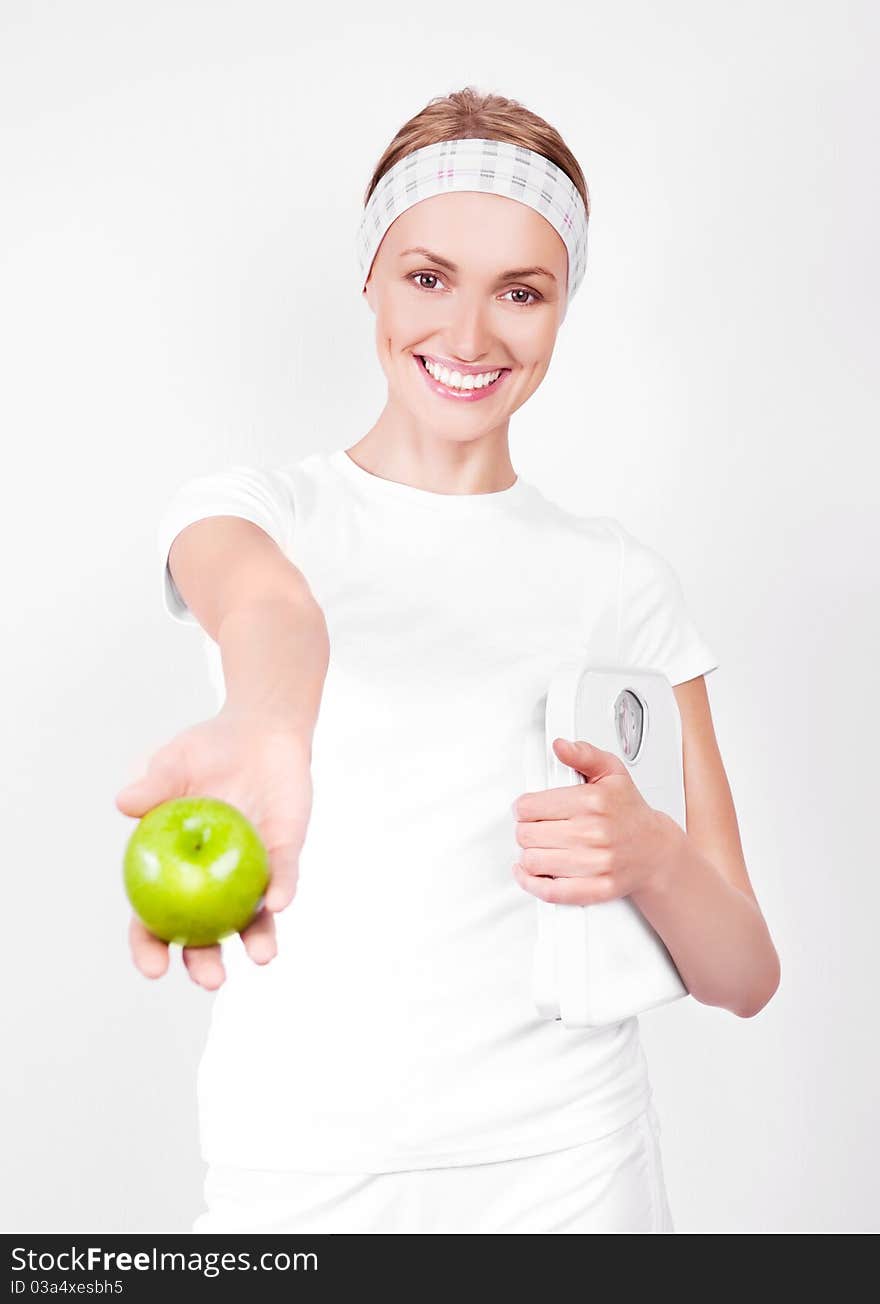 Beautiful young blond sporty woman  holding scales  and giving us a green apple. Beautiful young blond sporty woman  holding scales  and giving us a green apple