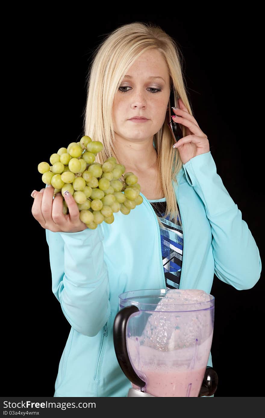 A woman is talking on the phone and making a smoothie holding grapes. A woman is talking on the phone and making a smoothie holding grapes.