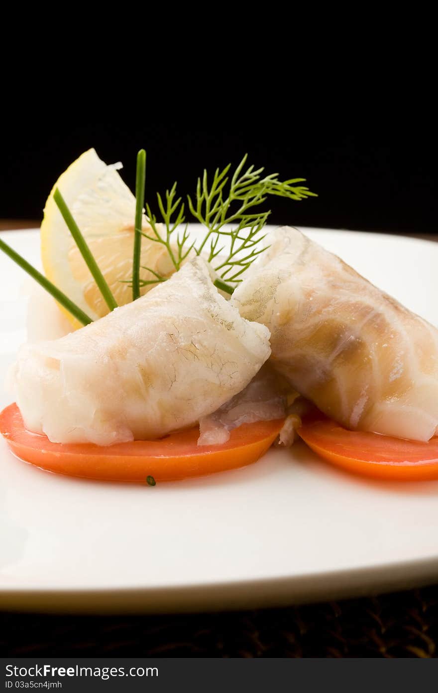 Photo of delicious sea bass rolls on sliced tomatoes. Photo of delicious sea bass rolls on sliced tomatoes