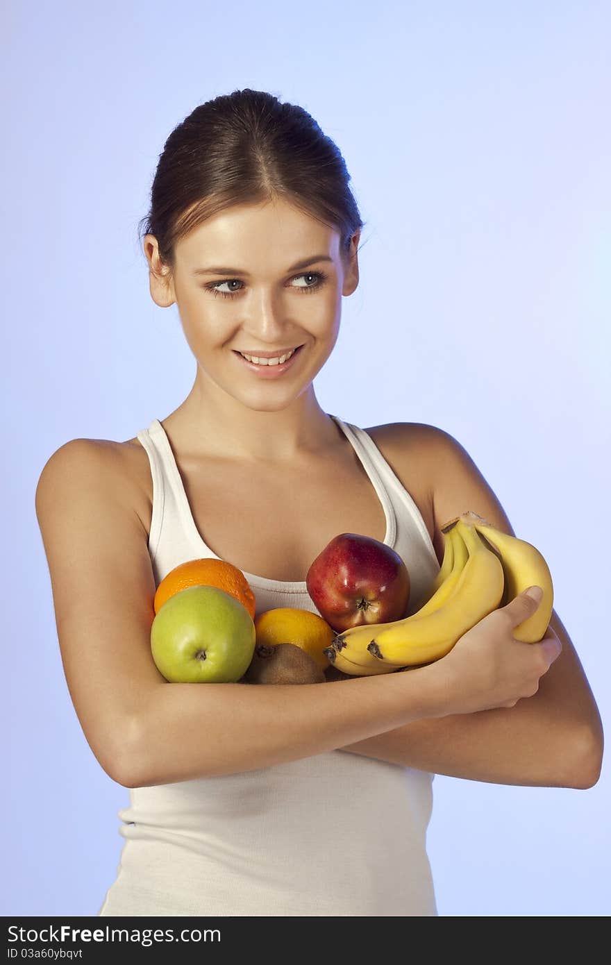 Young beautiful brunette is holding fruit on blue background isolated