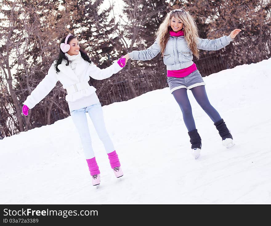 Two beautiful girls ice skating outdoor on a warm winter day (focus on the blond girl)