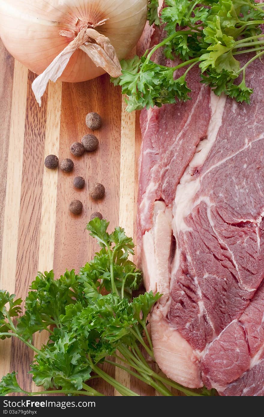 A piece of raw meat on a multilayer wooden kitchen cutting board.