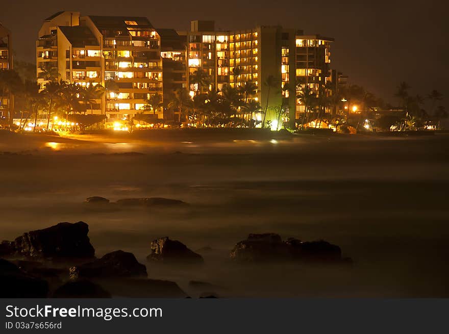 Beautiful ocean sea rocks with misty fog and an illuminated ocean-view hotel resort and city off in the distance on the horizon. Beautiful ocean sea rocks with misty fog and an illuminated ocean-view hotel resort and city off in the distance on the horizon.