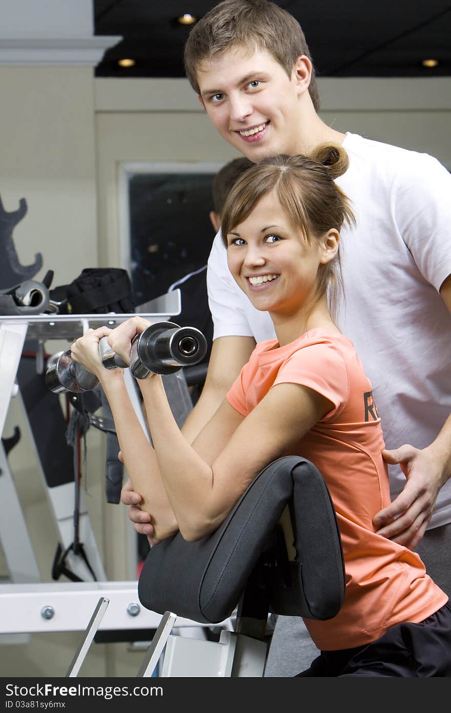 A girl's trainer shows the correct form of exercise with dumbbel. A girl's trainer shows the correct form of exercise with dumbbel