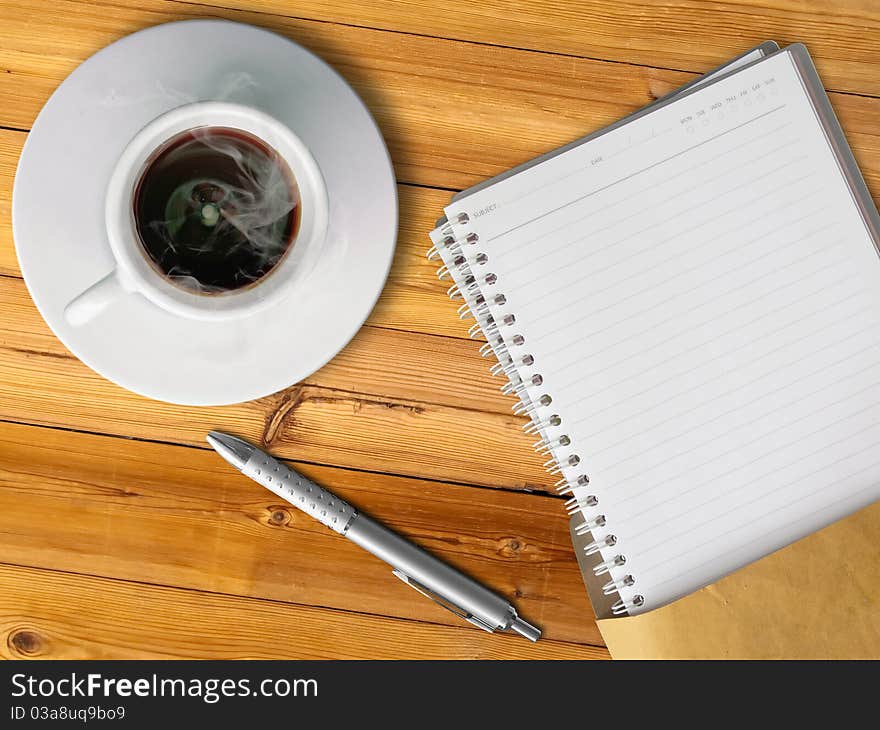 White cup of hot coffee and blank page note book on wood table with silver pen