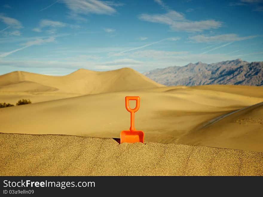 One single toy shovel stands against a sea of sand. One single toy shovel stands against a sea of sand.