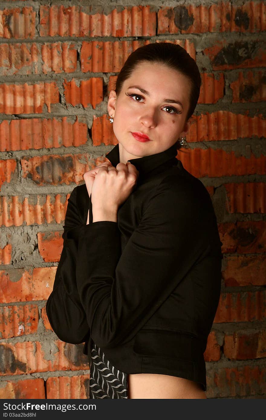 Girl in black suit posing at red brickwall.