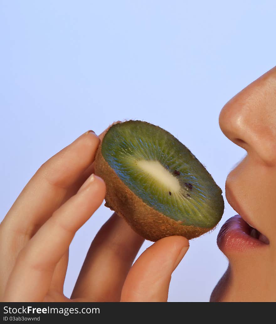 Young woman enjoying a slice of kiwi on blue background