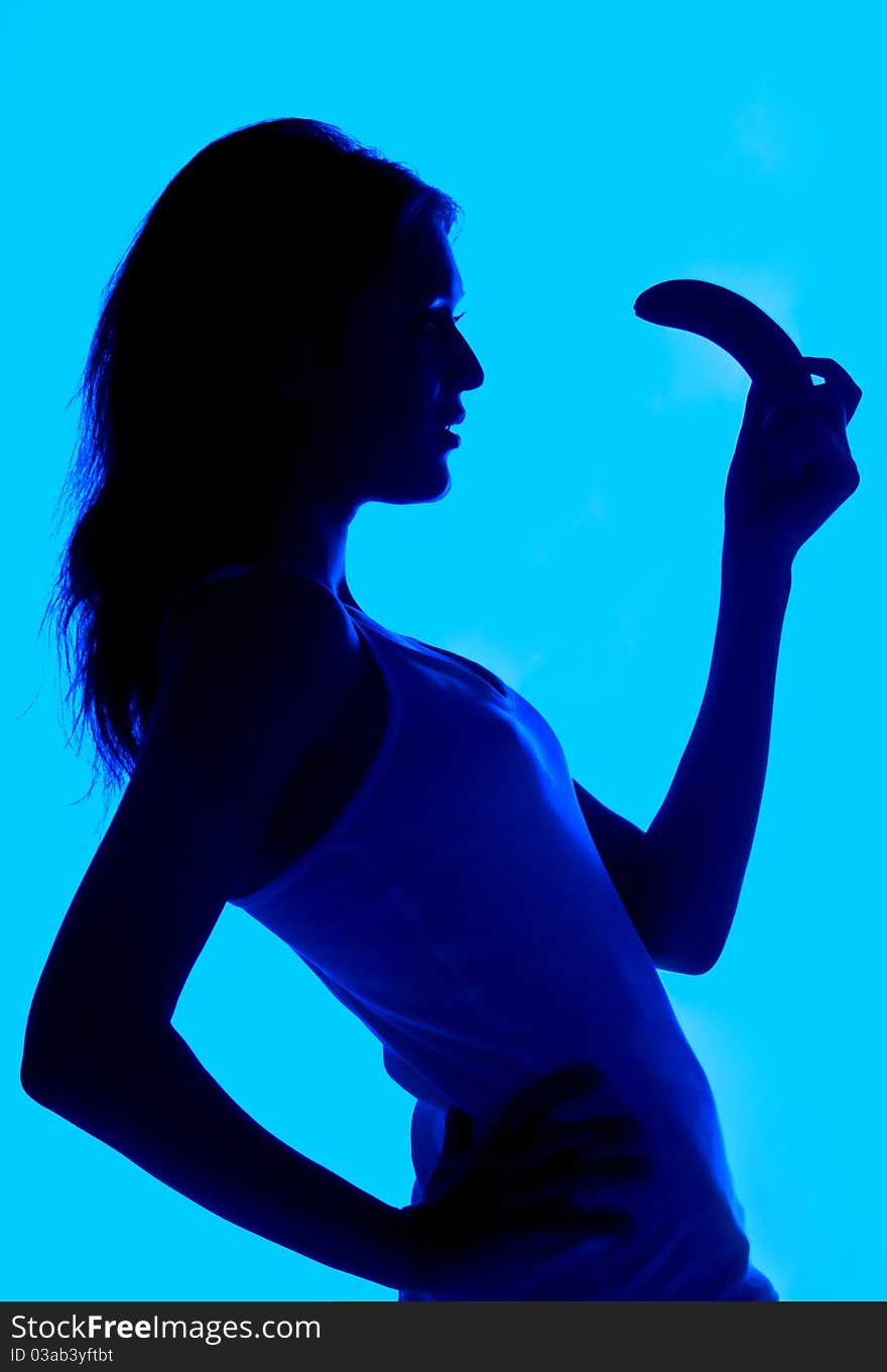 Silhouette of the woman with a banana in a hand on a blue background the isolated