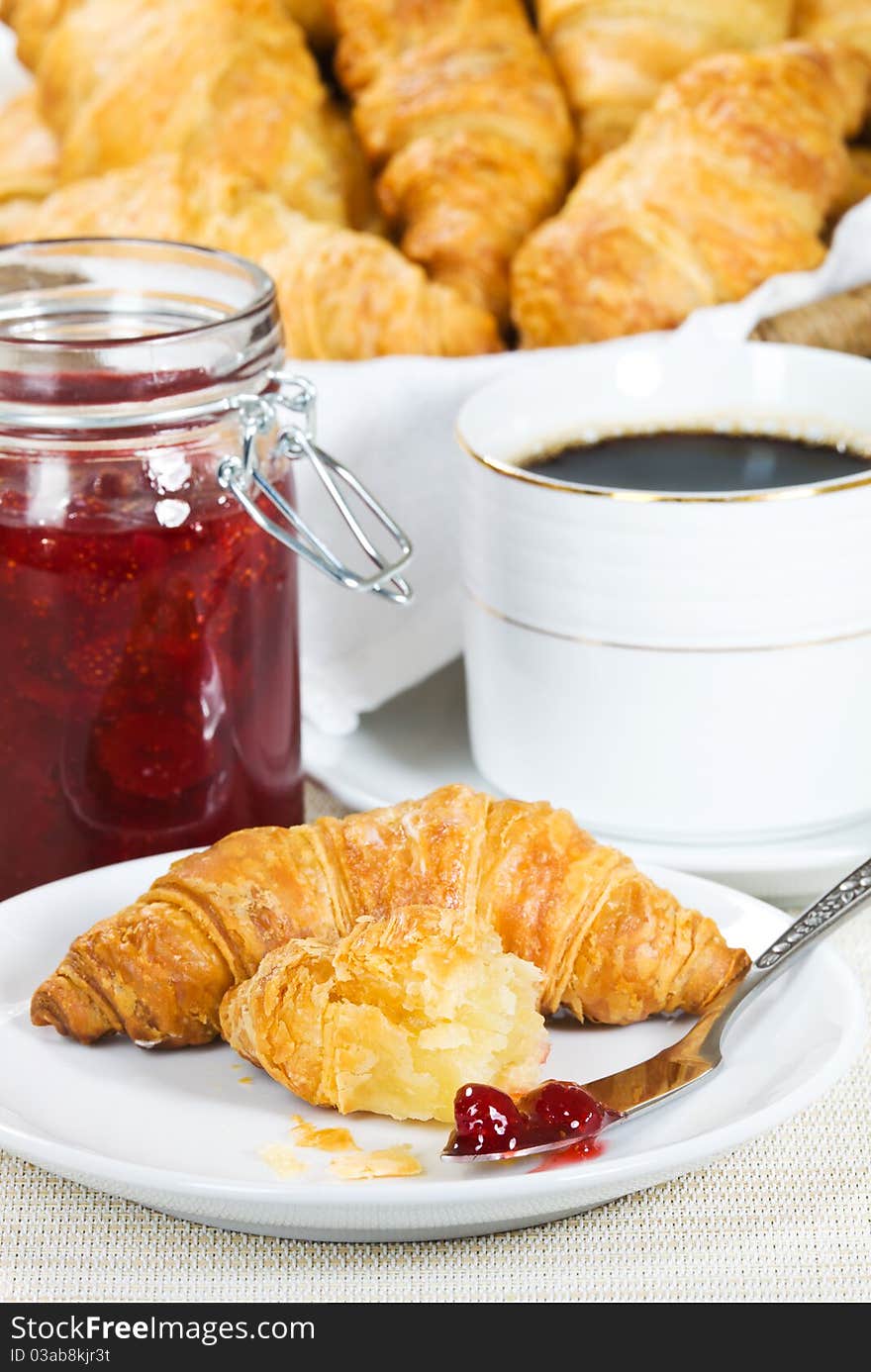 Croissant breakfast in a plate. Strawberry jam and black coffee in the background. Shallow depth of field. Croissant breakfast in a plate. Strawberry jam and black coffee in the background. Shallow depth of field.