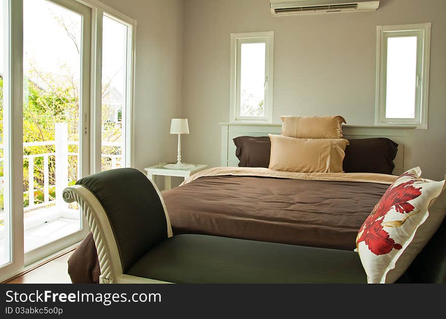 White bedroom with brown sheet bed and couch shot from foot