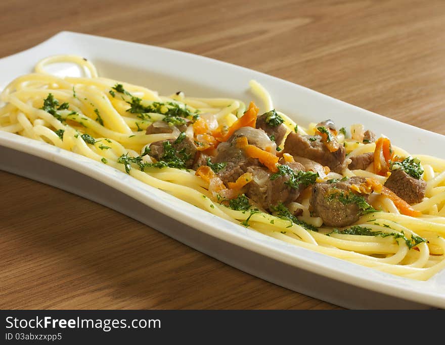 Spaghetti with meat and greens on a long white plate