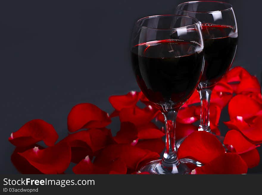 Two glasses of wine with petals of red rose