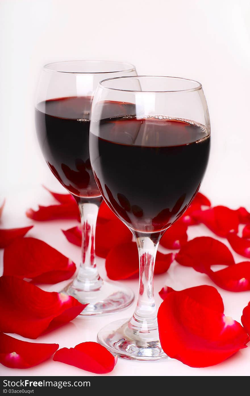 Two glasses of wine with petals of red rose