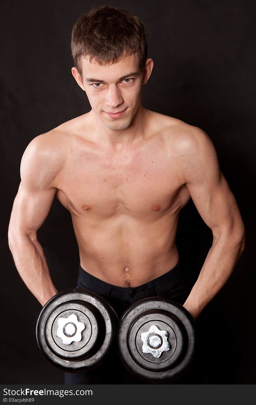 Portrait of an energetic naked man lifting dumbbell against black background