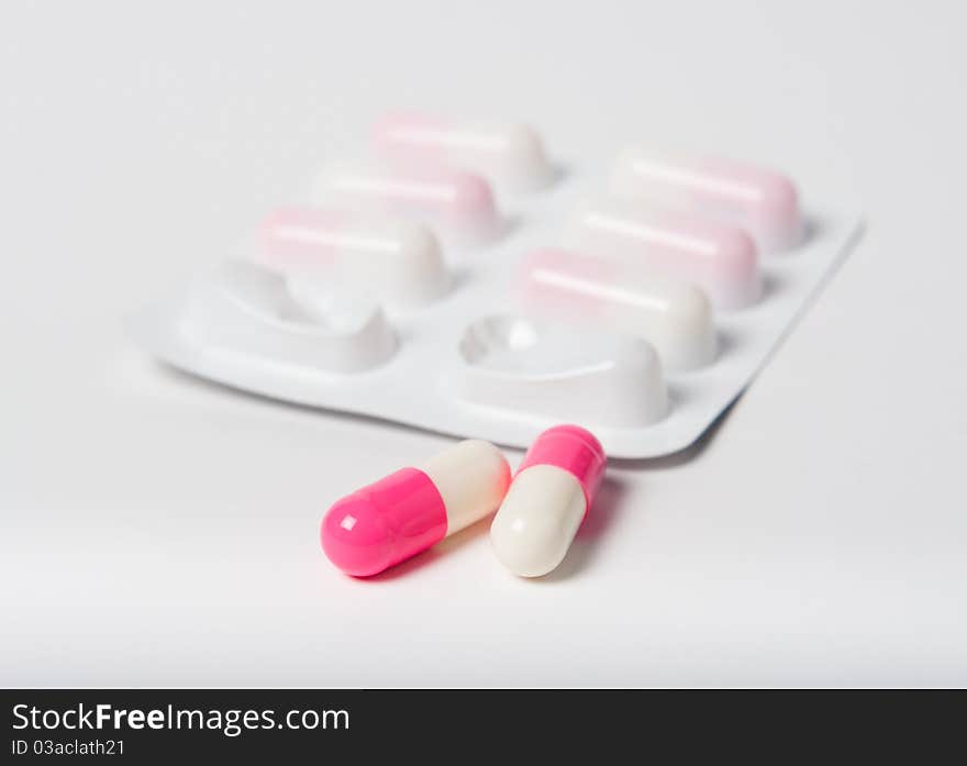 Pink pharmaceutical capsules with packaging close up on white with focus on pills. Pink pharmaceutical capsules with packaging close up on white with focus on pills