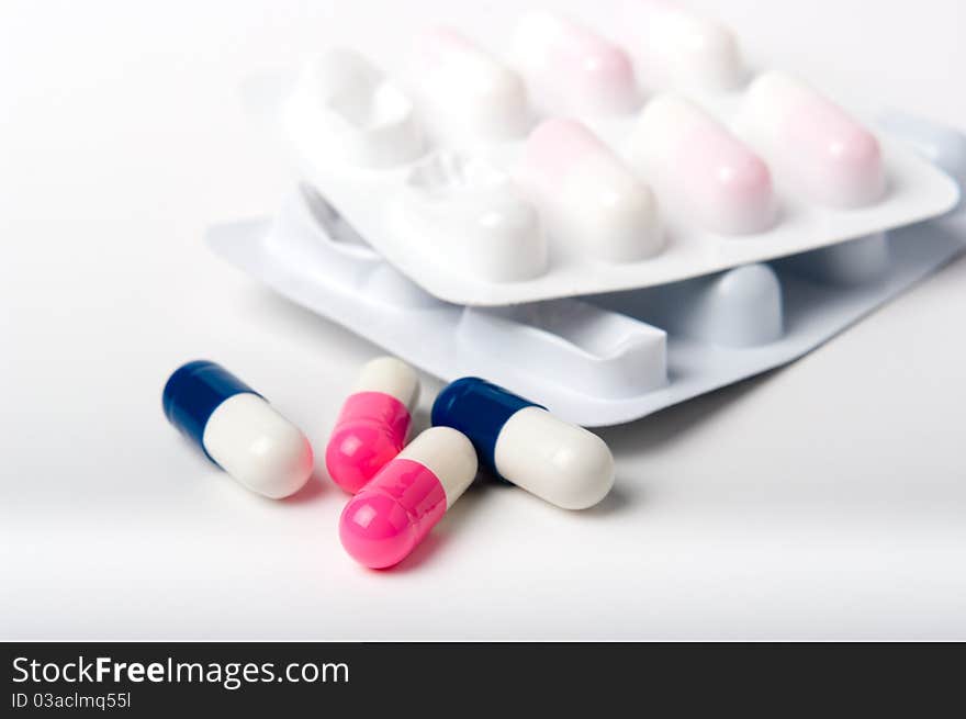 Blue and pink pharmaceutical capsules with blister packs on white close up. Blue and pink pharmaceutical capsules with blister packs on white close up