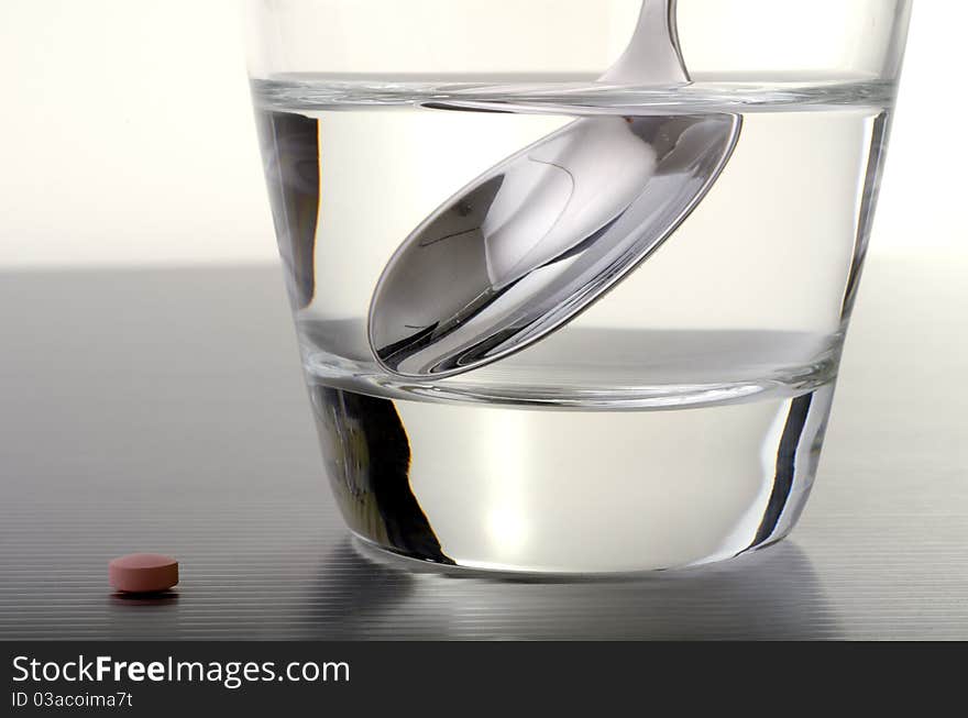 Pill next to a glass of water with a teaspoon