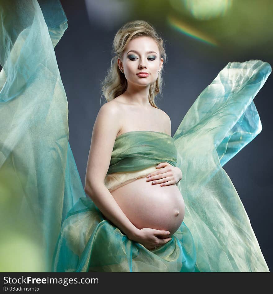 Beautiful pregnant woman in green cloth on grey background