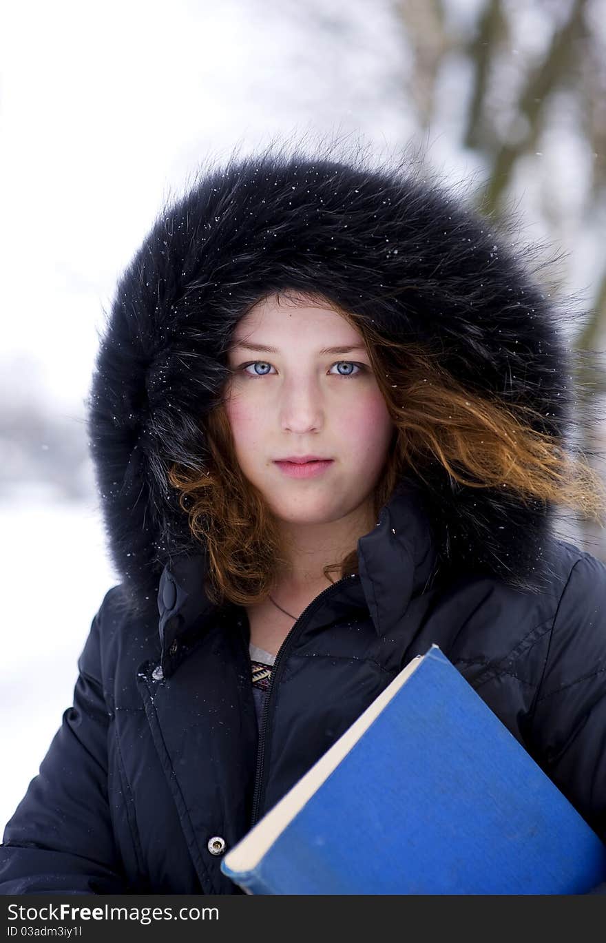 Young girl in the hood with blue book in winter time