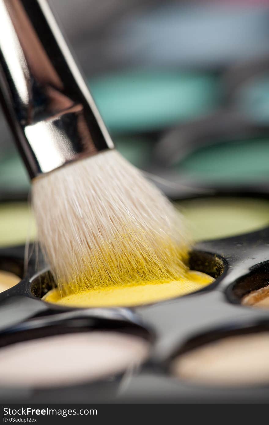 A close-up image of a eye-shadow set, with a professional makeup brush picking up some yellow colour. A close-up image of a eye-shadow set, with a professional makeup brush picking up some yellow colour