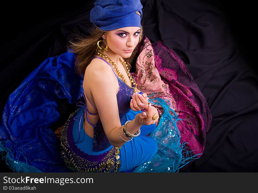 Beautiful girl in a turban and a stylized ethnic costume sits on headscarves