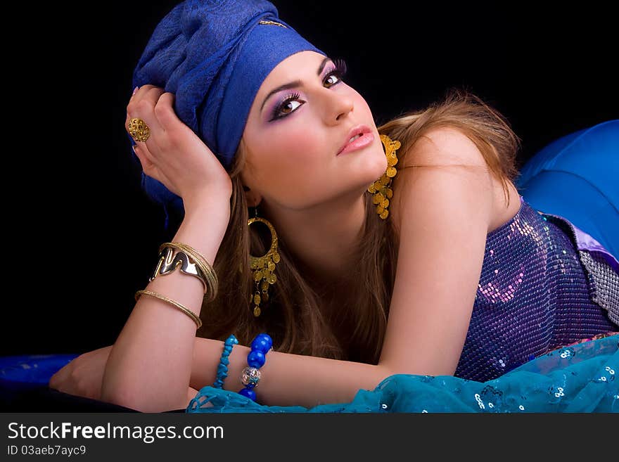 Beautiful girl in a turban and a stylized ethnic costume lies on headscarves