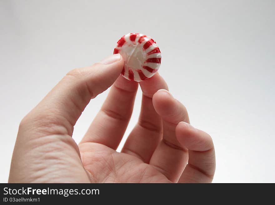 Hand holding a red and white peppermint.