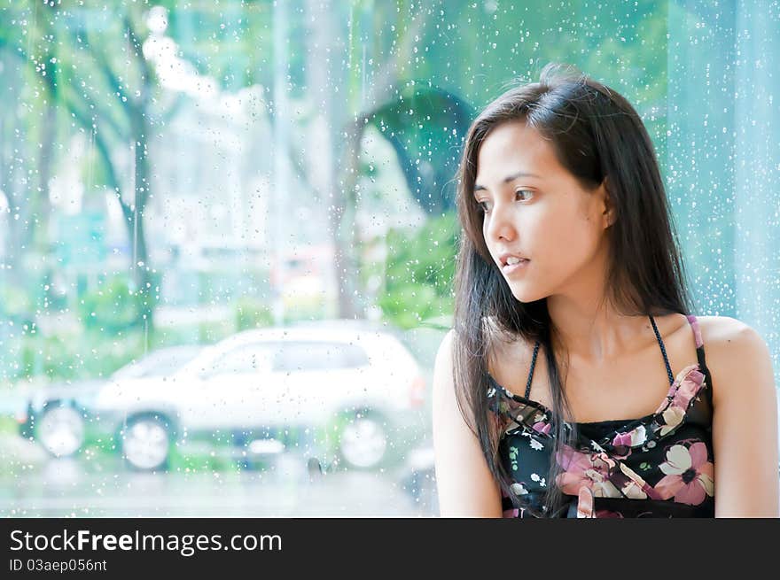 Young girl looking outside wet window