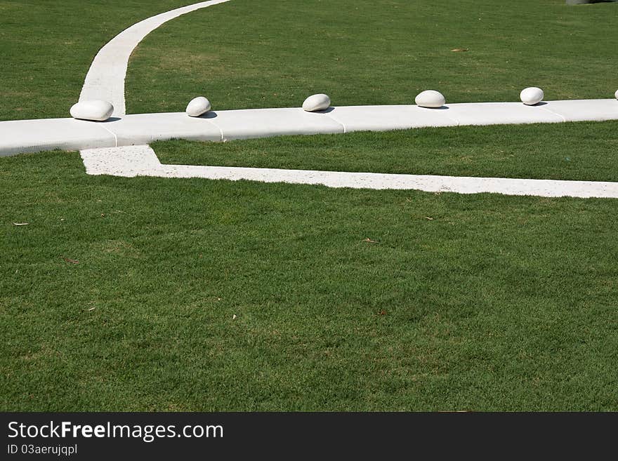 White park path through grass evoking Euro symbol. Copy space on green at bottom suitable for eco-friendly text. White polished stones evenly spaced through the middle. White park path through grass evoking Euro symbol. Copy space on green at bottom suitable for eco-friendly text. White polished stones evenly spaced through the middle.