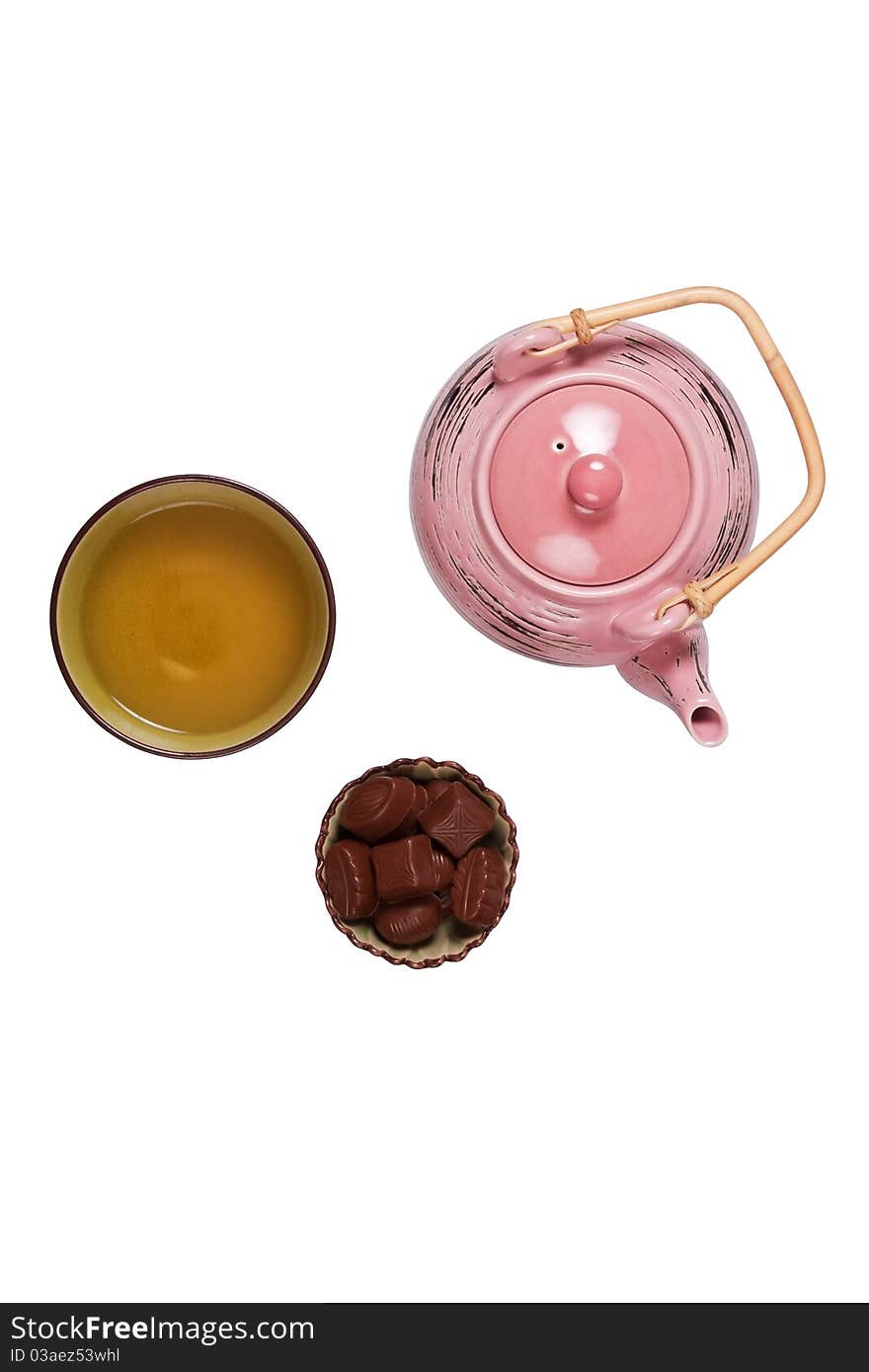 Composition with tea set that shows teakettle, tea in a cup and candies in a bowl on a white background with shadows.