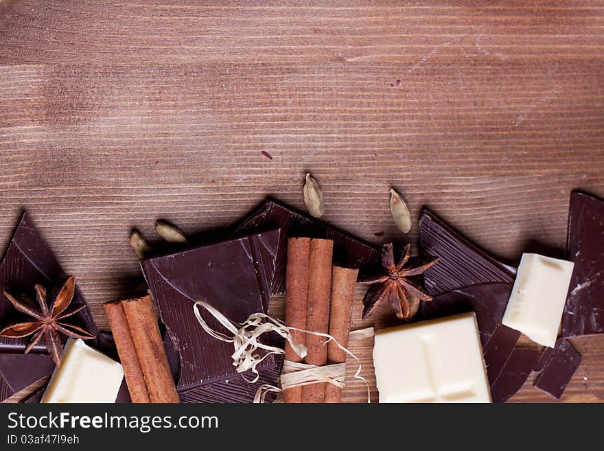 Border of chopped black and white chocolate with cinnamon, anise and cardamom on wooden table. Border of chopped black and white chocolate with cinnamon, anise and cardamom on wooden table