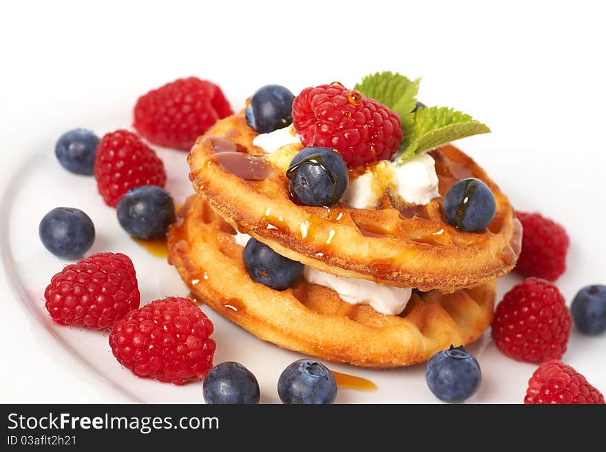 Belgian waffles with fresh raspberries, blueberries, mint leaves and cream on white plate. Belgian waffles with fresh raspberries, blueberries, mint leaves and cream on white plate