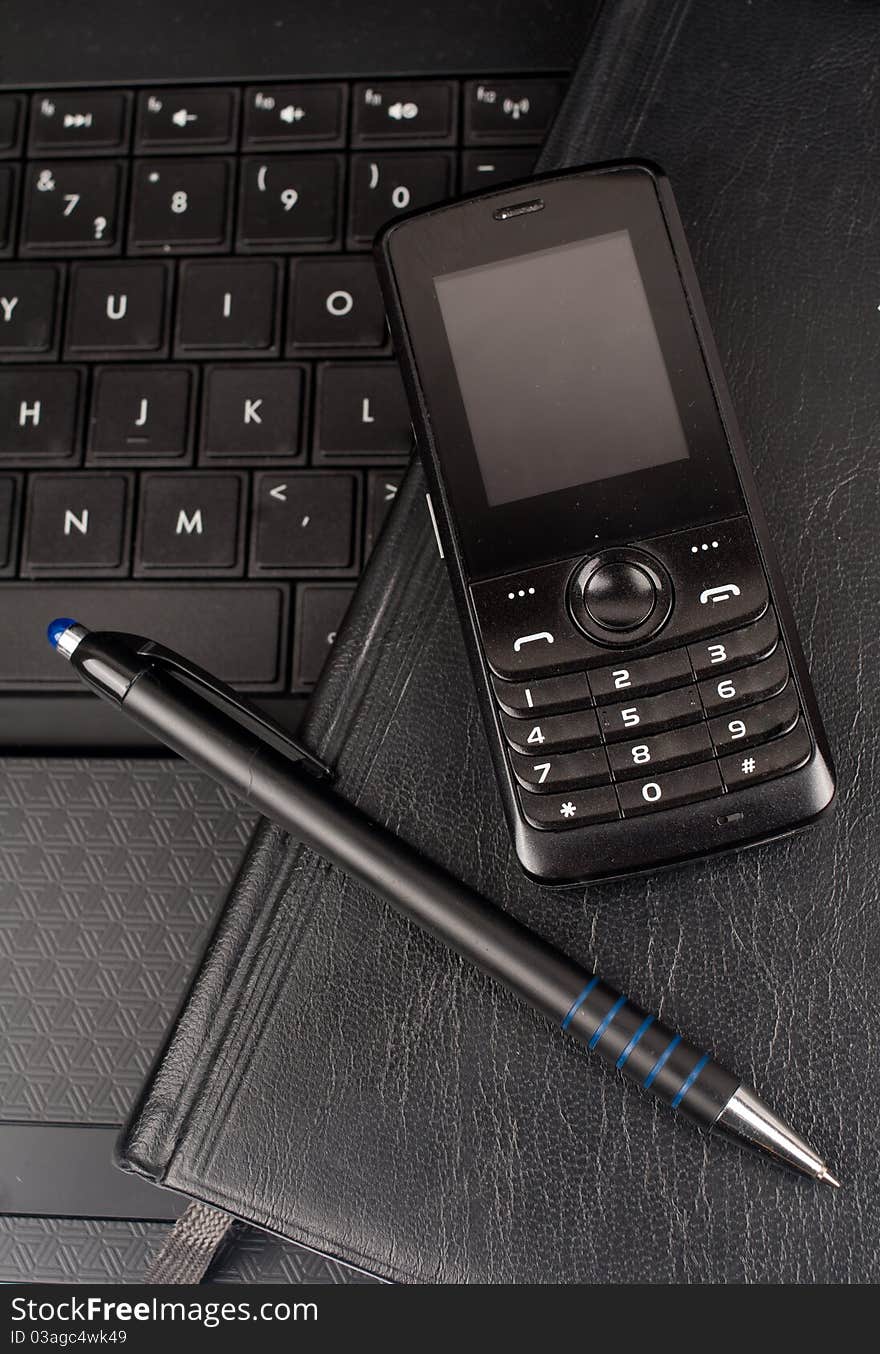 Closeup of black laptop, pen, mobile phone together. Closeup of black laptop, pen, mobile phone together