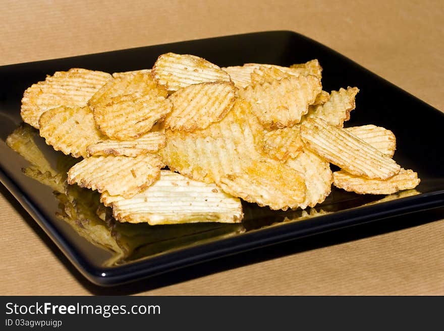 Crinkle potato crisps on a square plate against a brown background. Crinkle potato crisps on a square plate against a brown background