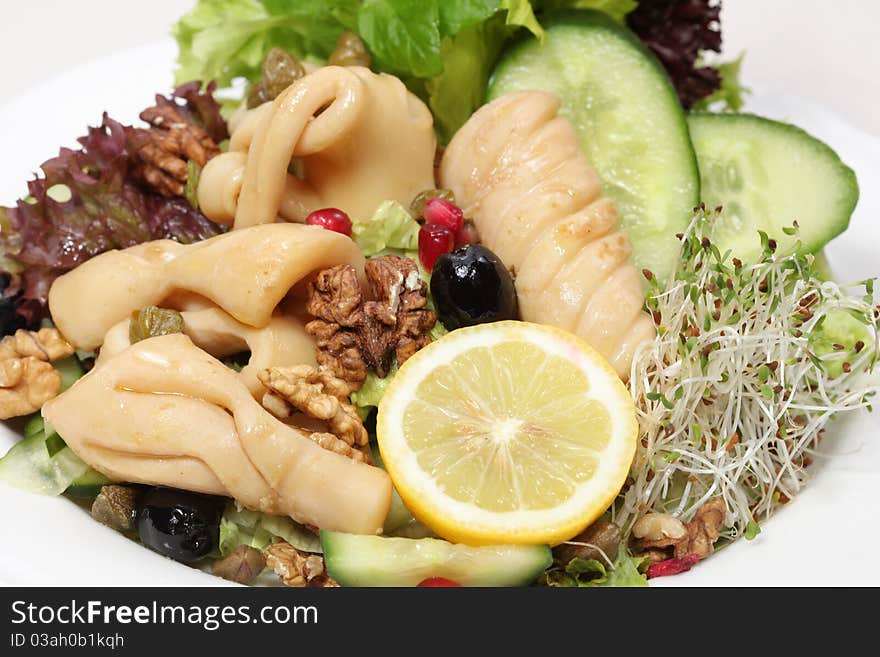 Squid in company of lemon and tomatoes served on a plate with nuts, garlic, butter and parsley. Squid in company of lemon and tomatoes served on a plate with nuts, garlic, butter and parsley.