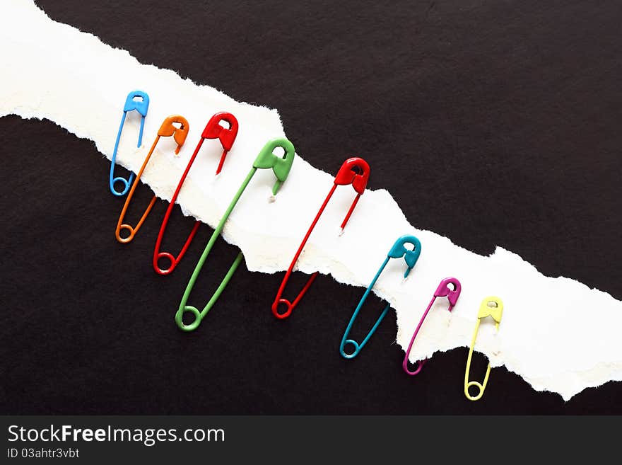 Set of color safety pins constrained to disrupt white paper on black background