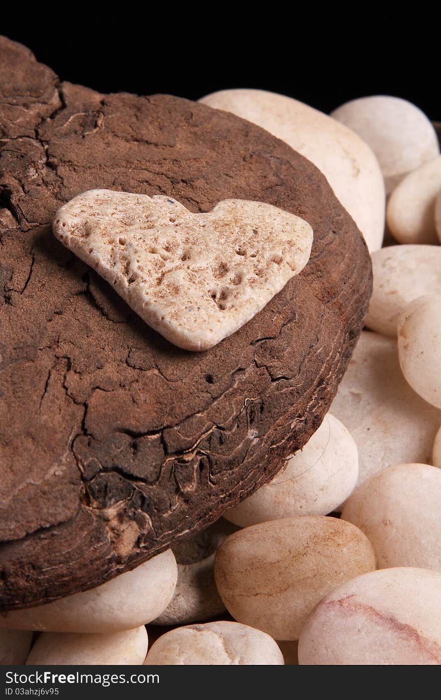 Stone heart on top of a piece of smooth bark, some white pebbles are seen below. Stone heart on top of a piece of smooth bark, some white pebbles are seen below.