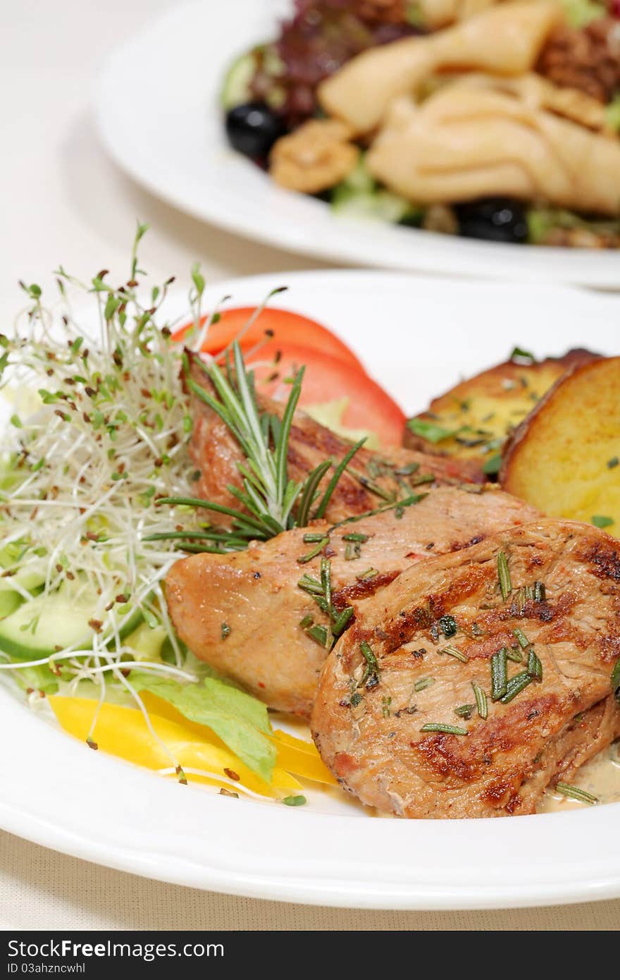 Chicken in company of baked potatoes and cucumber served on a plate with garlic, butter and parsley. Chicken in company of baked potatoes and cucumber served on a plate with garlic, butter and parsley.