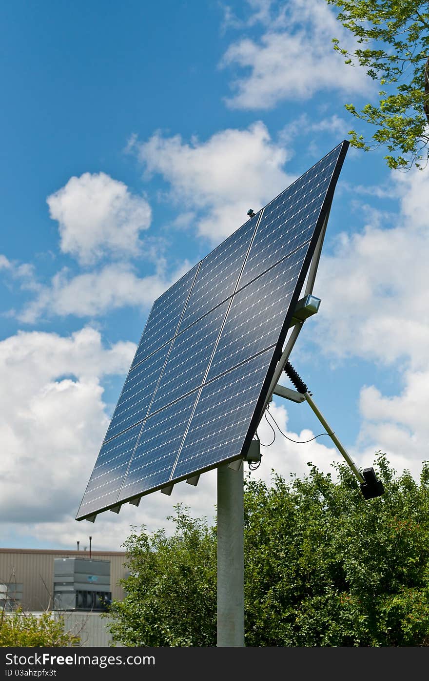 A photovoltaic solar panel array with a blue sky and green leaves in the background. A photovoltaic solar panel array with a blue sky and green leaves in the background.