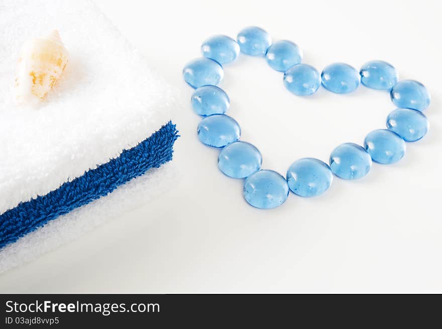 A tower of white and blue towels, shell and the heart of inlaid blue stone on a white background. A tower of white and blue towels, shell and the heart of inlaid blue stone on a white background