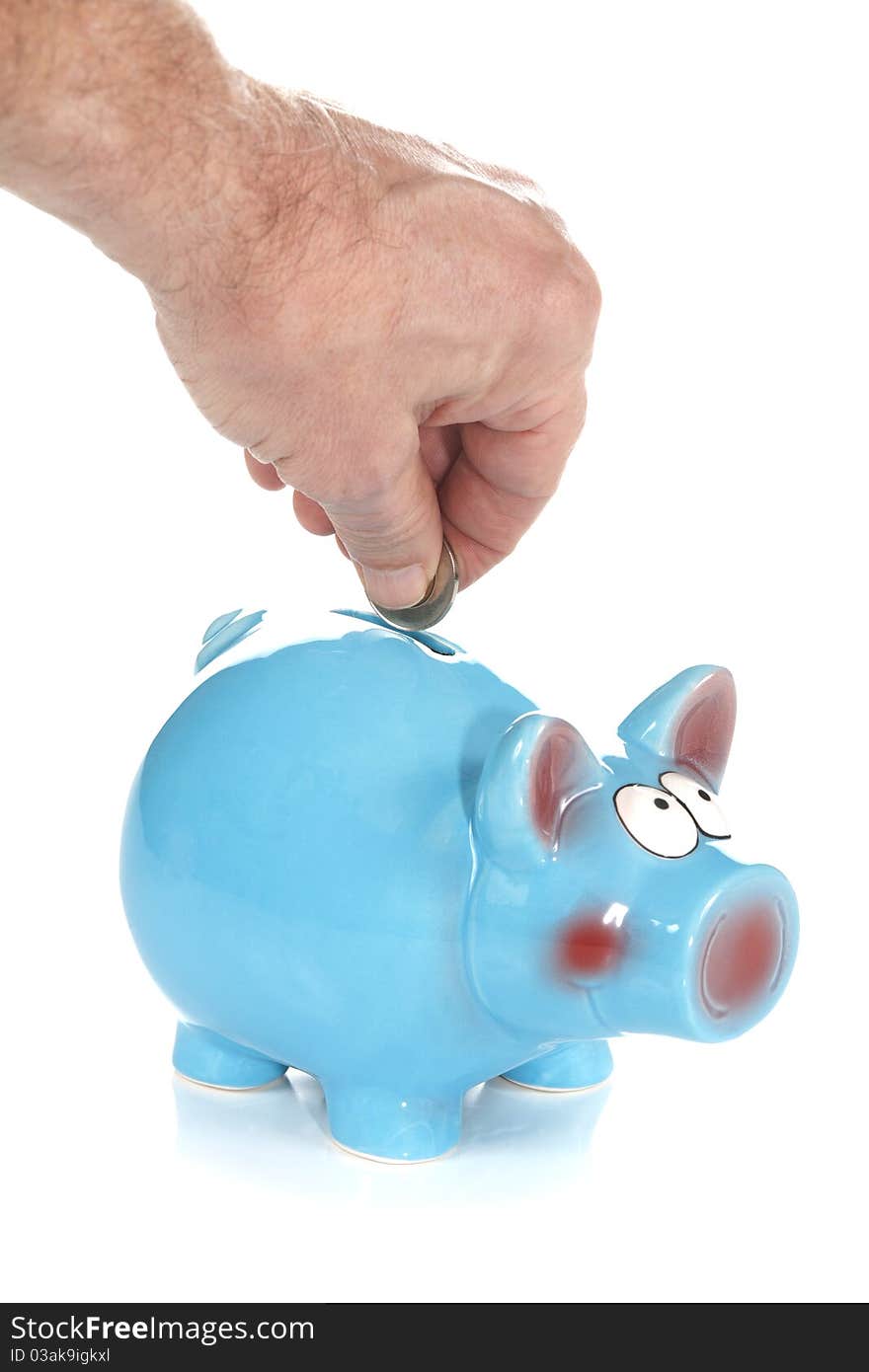 A front studio isolation shot on a white background of a coin being dropped into a blue ceramic piggy bank. A front studio isolation shot on a white background of a coin being dropped into a blue ceramic piggy bank.