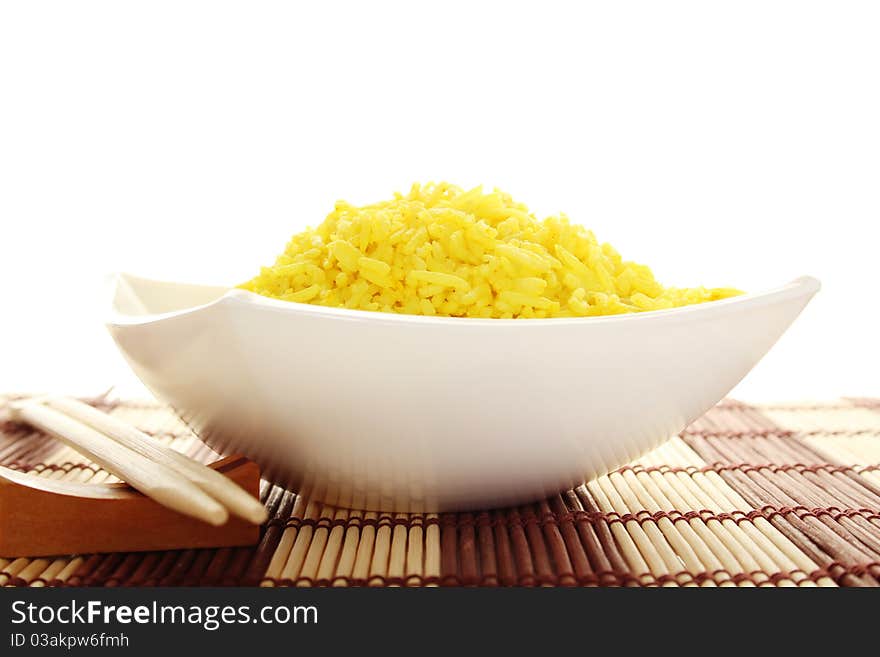 Boiled yellow rice and a white plate beside lie wooden sticks. Plate stands on a wooden mat. Isolated on a white background. Boiled yellow rice and a white plate beside lie wooden sticks. Plate stands on a wooden mat. Isolated on a white background