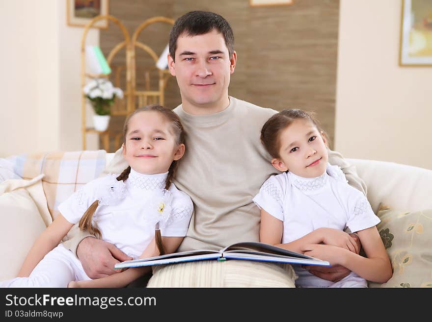 A father with her daughters at home in the living room reading a book. A father with her daughters at home in the living room reading a book