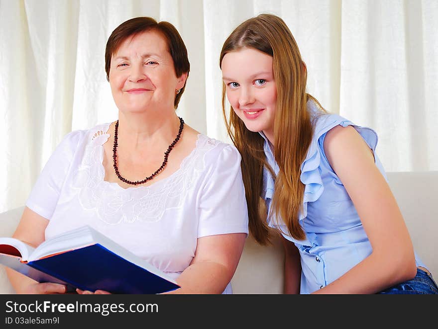 A grandmother with her young granddaughter together sitting on a sofa