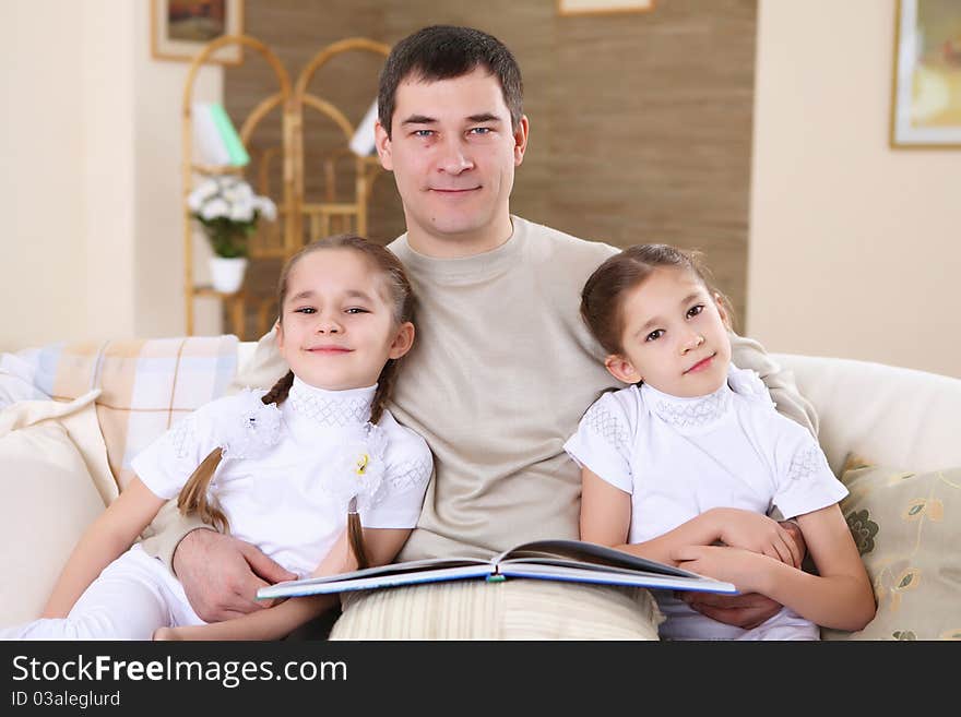 A father with her daughters at home in the living room reading a book. A father with her daughters at home in the living room reading a book