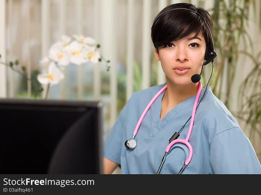 Smiling Attractive Multi-ethnic Young Woman Wearing Headset, Scrubs and Stethoscope Near Her Computer Monitor. Smiling Attractive Multi-ethnic Young Woman Wearing Headset, Scrubs and Stethoscope Near Her Computer Monitor.