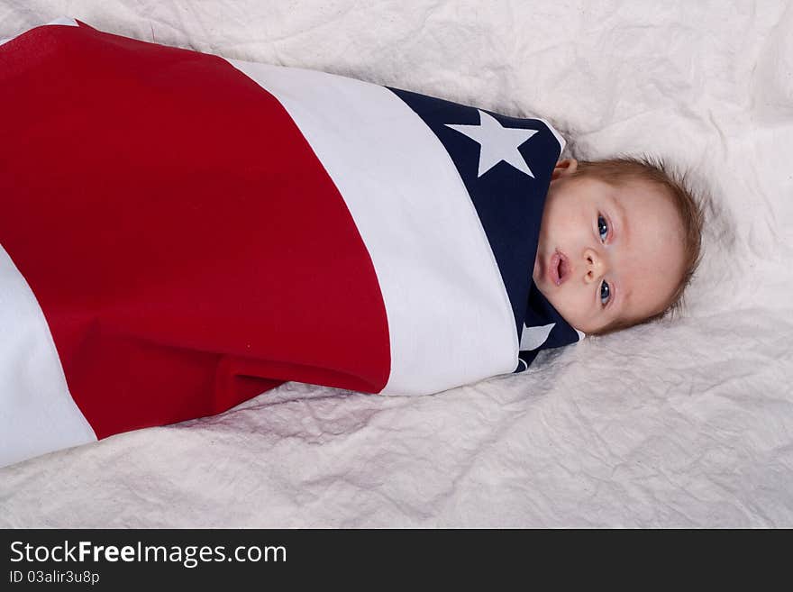 A baby swattled in an american flag fabric/blanket. A baby swattled in an american flag fabric/blanket.